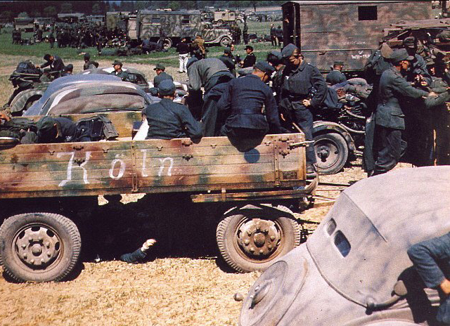 [Photo 8 - German infantry and motorized vehicles at what seems to be a staging area. The most interesting thing about this photograph (which must have been taken sometime after the 1943 order) is the extremely wide variety one finds in all the camouflage applications and colours! Some clearly use Dunkelbraun, for instance, where as other seems to eschew all brown colors and go for green, and the vehicle in the lower right corner is painted in what could be a desert pattern. This sort of variation was also reflected in how tanks were painted by the maintenance crews.]
